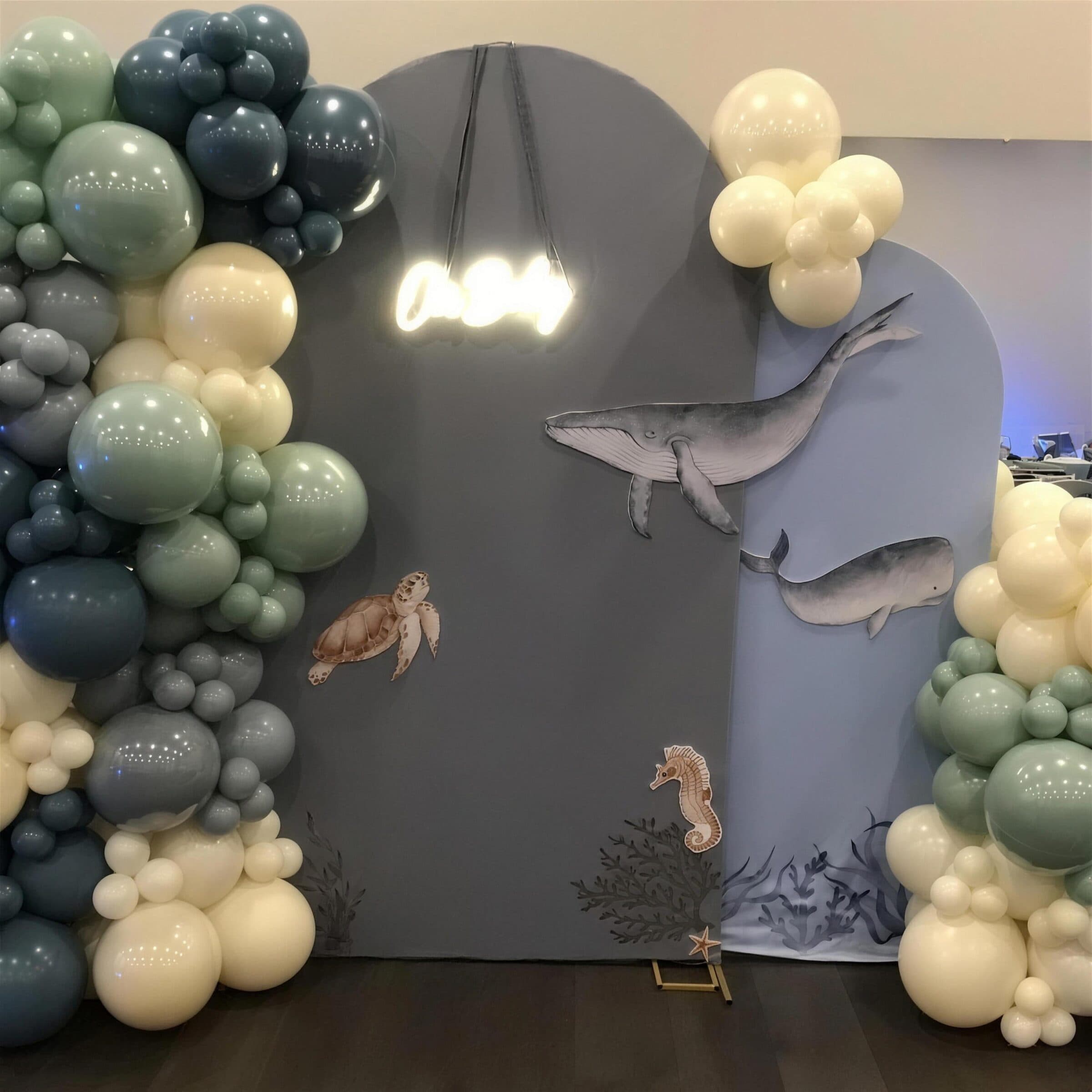 Under-the-sea backdrop with a whale, sea turtle and seahorse on arch panels, ringed by sage and cream balloon garlands at a baby shower at The Cove at St. Johns, near Jacksonville, FL
