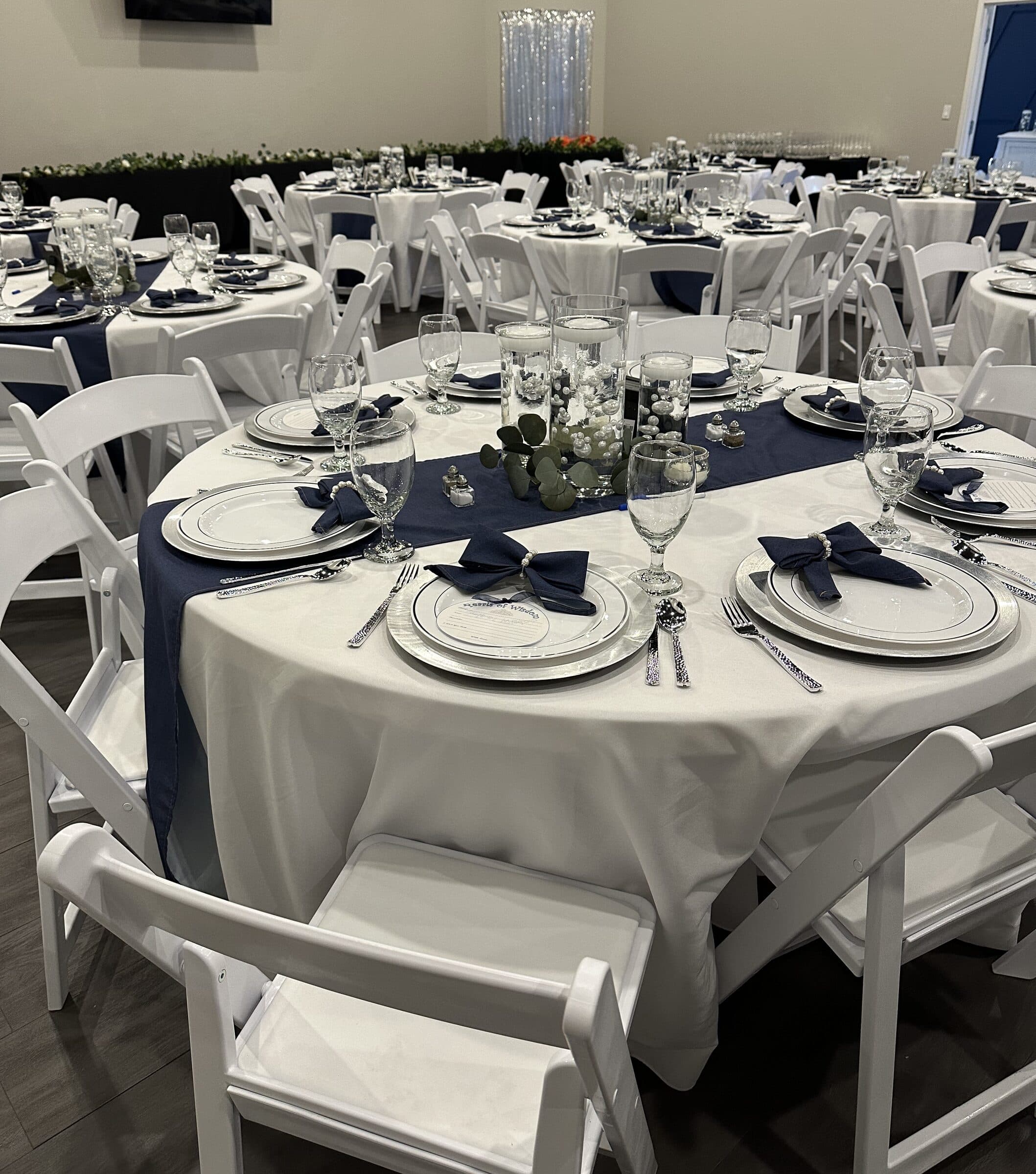 Navy and silver reception at The Cove at St. Johns, St. Johns County FL - round tables with navy runners, floating candles over white pearls, silver-rim chargers and a greenery-topped head table